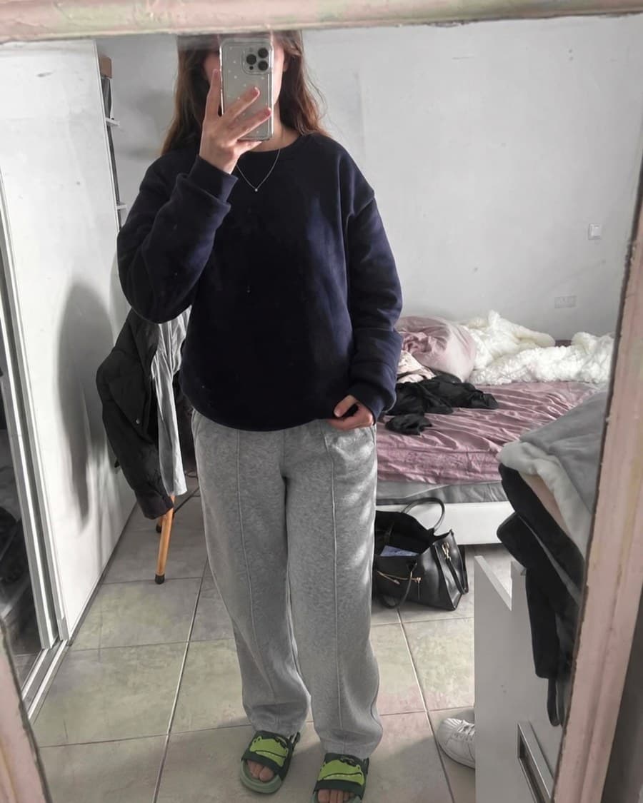 Les claquettes portées devant un miroir, avec un sweat marine et un pantalon gris.