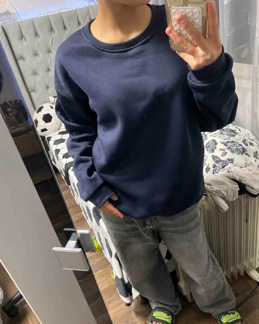 Les claquettes portées devant un miroir, avec un sweat marine et un jean gris.