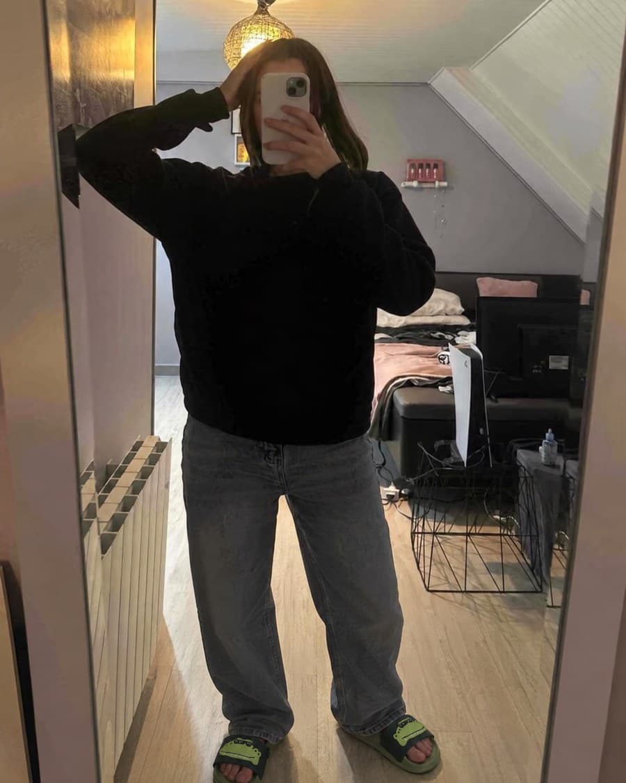 Les claquettes portées devant un miroir, avec un sweat noir et un jean.