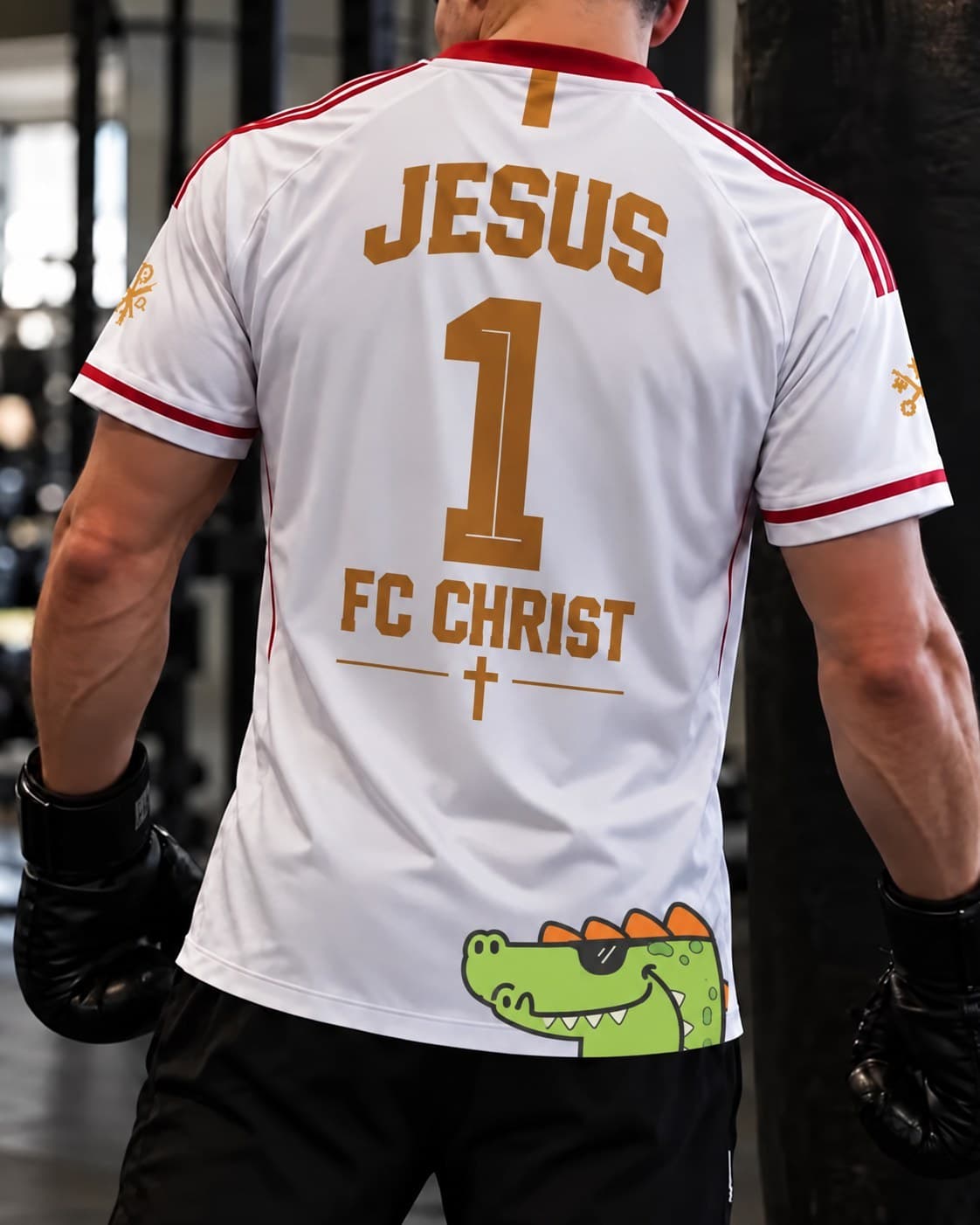 Un maillot blanc porté de dos dans une salle de boxe, floqué « Jesus 1 — FC Christ », un crocodile à lunettes sur le bas.